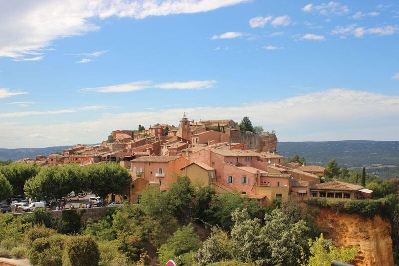 Paysage provençal avec des maisons aux façades couleur peinture ocre sous un ciel bleu clair